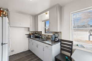 Kitchen with freestanding refrigerator, white cabinetry, dark wood-style floors, and backsplash