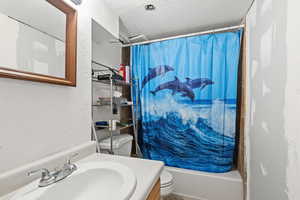 Full bathroom featuring a textured ceiling, a textured wall, vanity, and shower / tub combo