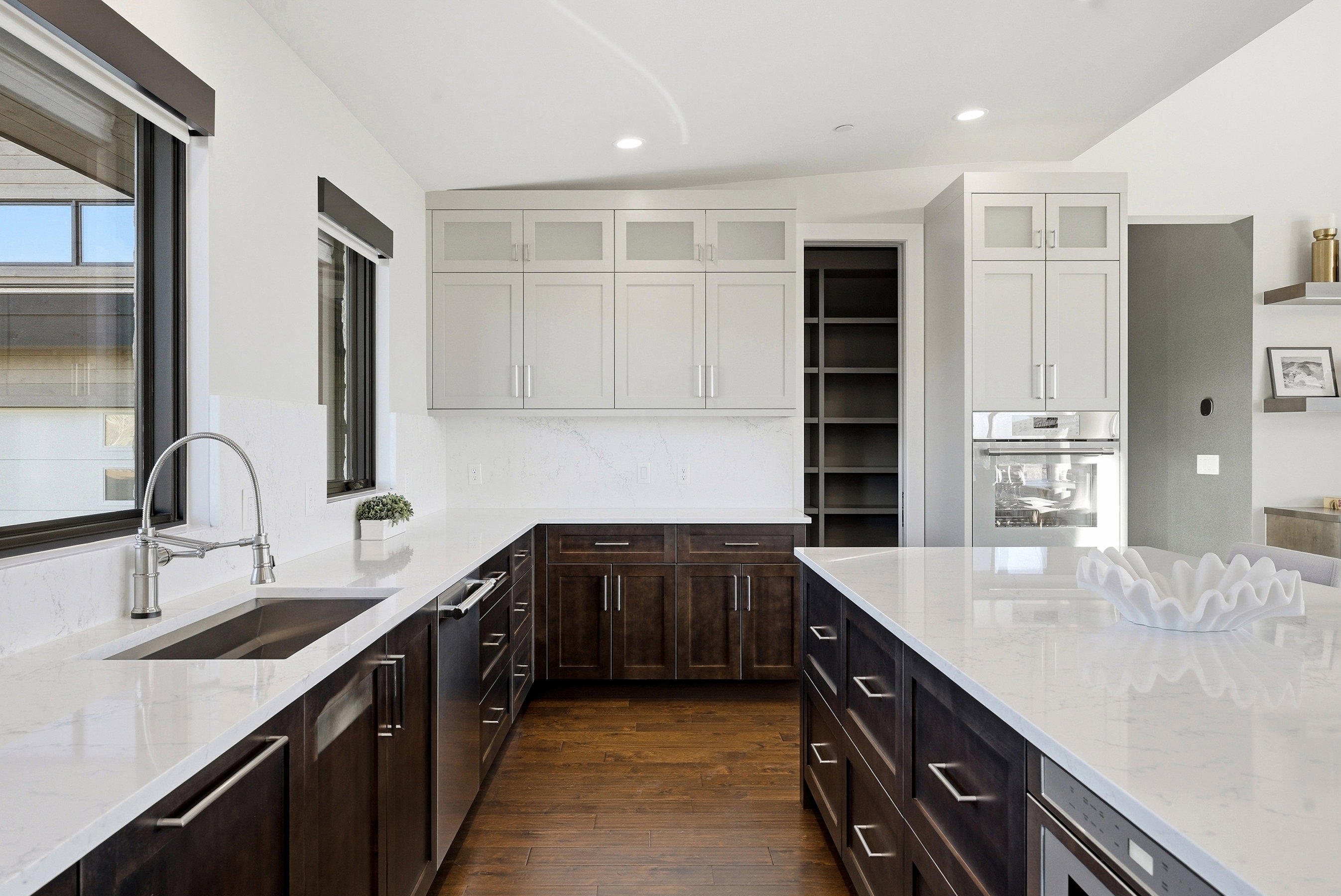 Modern kitchen featuring dark wood-finish base cabinetry, light upper cabinetry with frosted glass panels, stainless steel appliances, and light countertops