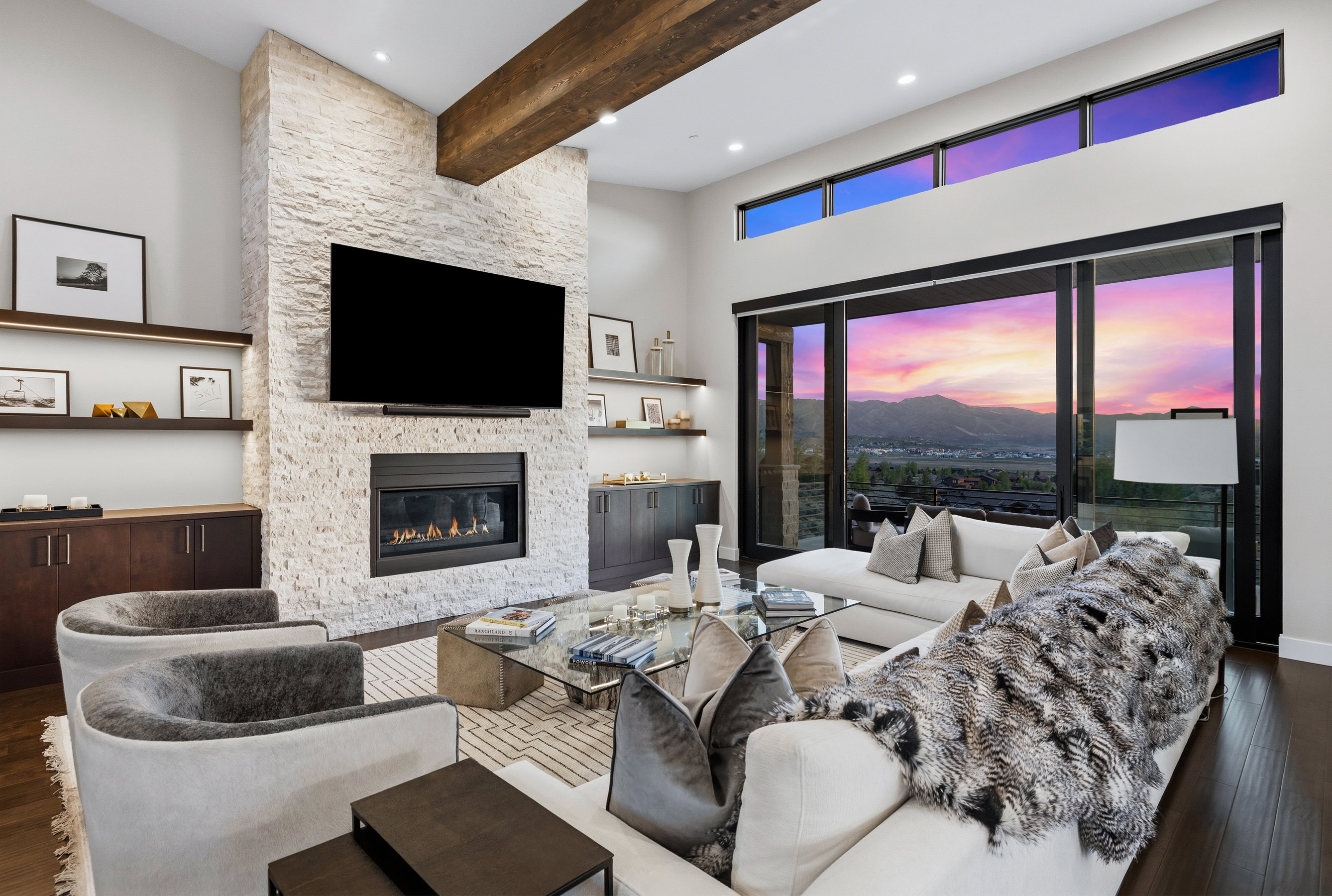 Spacious living area featuring a stacked stone fireplace, dark wood-finish flooring, and high ceilings with an exposed wood beam