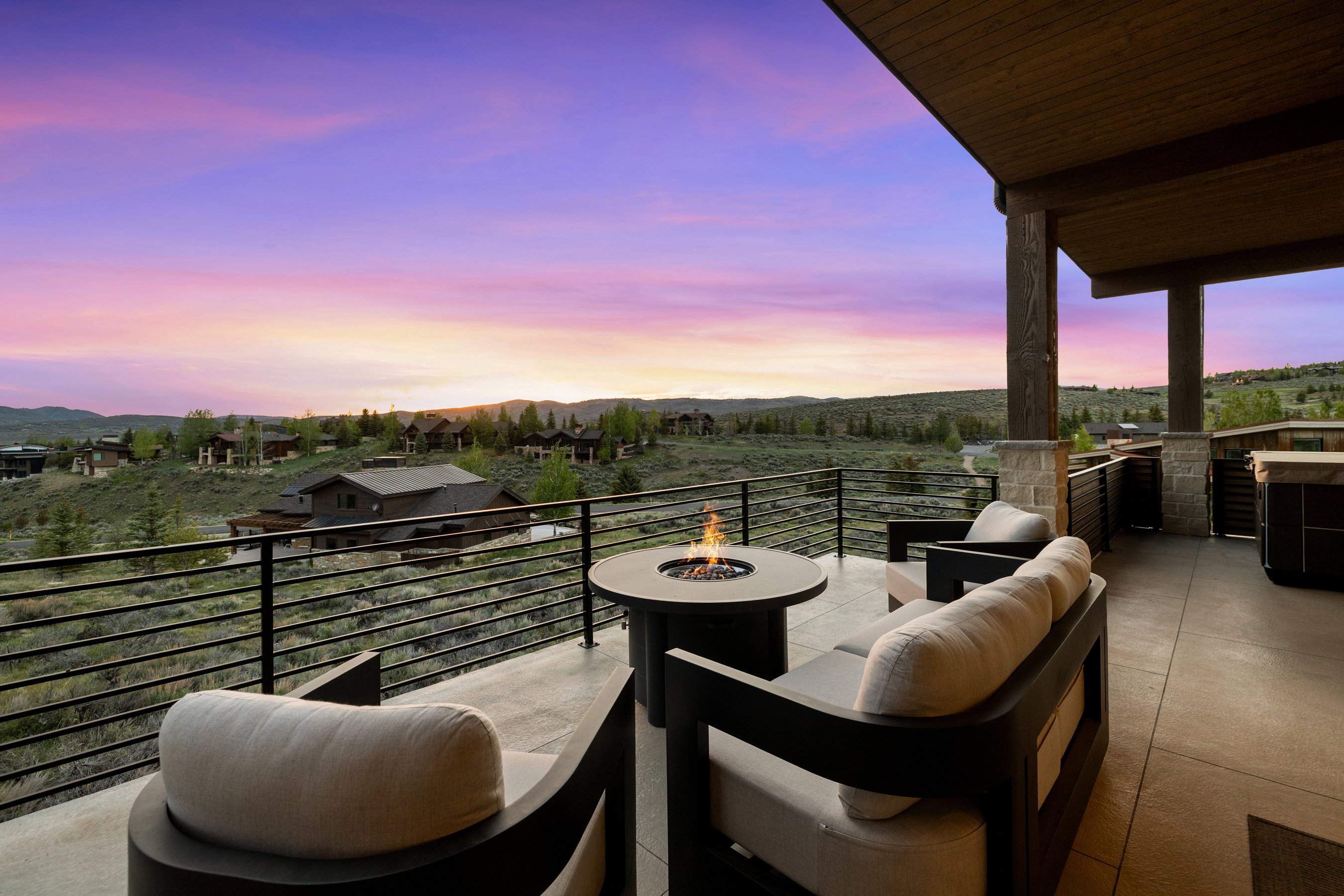 Expansive outdoor living area featuring a concrete patio, metal railing, and built-in fire pit