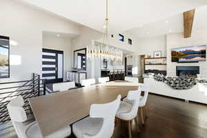 Dining area with dark wood-style flooring, a large fireplace, and a towering ceiling