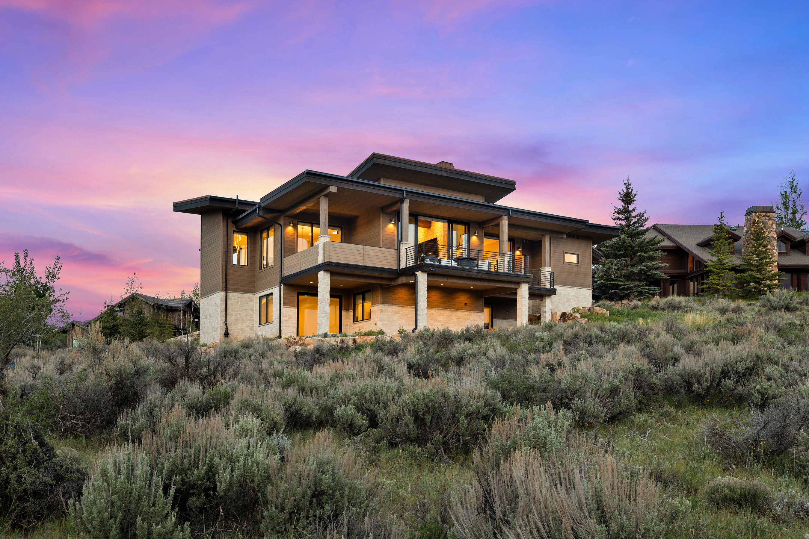 Contemporary multi-level residence featuring expansive windows, multiple outdoor balconies, and a stone and wood exterior