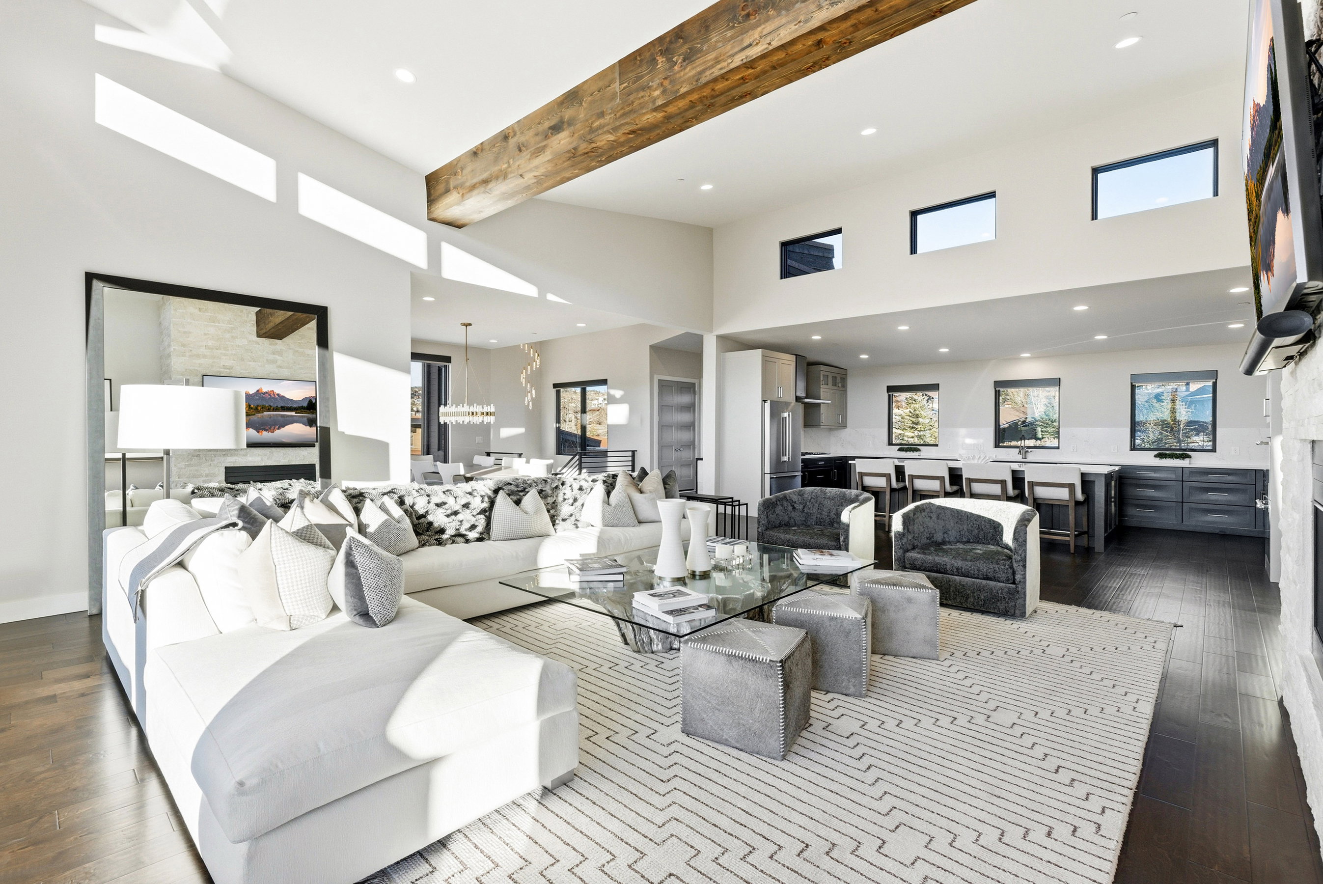 Expansive open concept living area featuring dark wood-finish flooring, a vaulted ceiling with exposed wood beam, and high transom windows