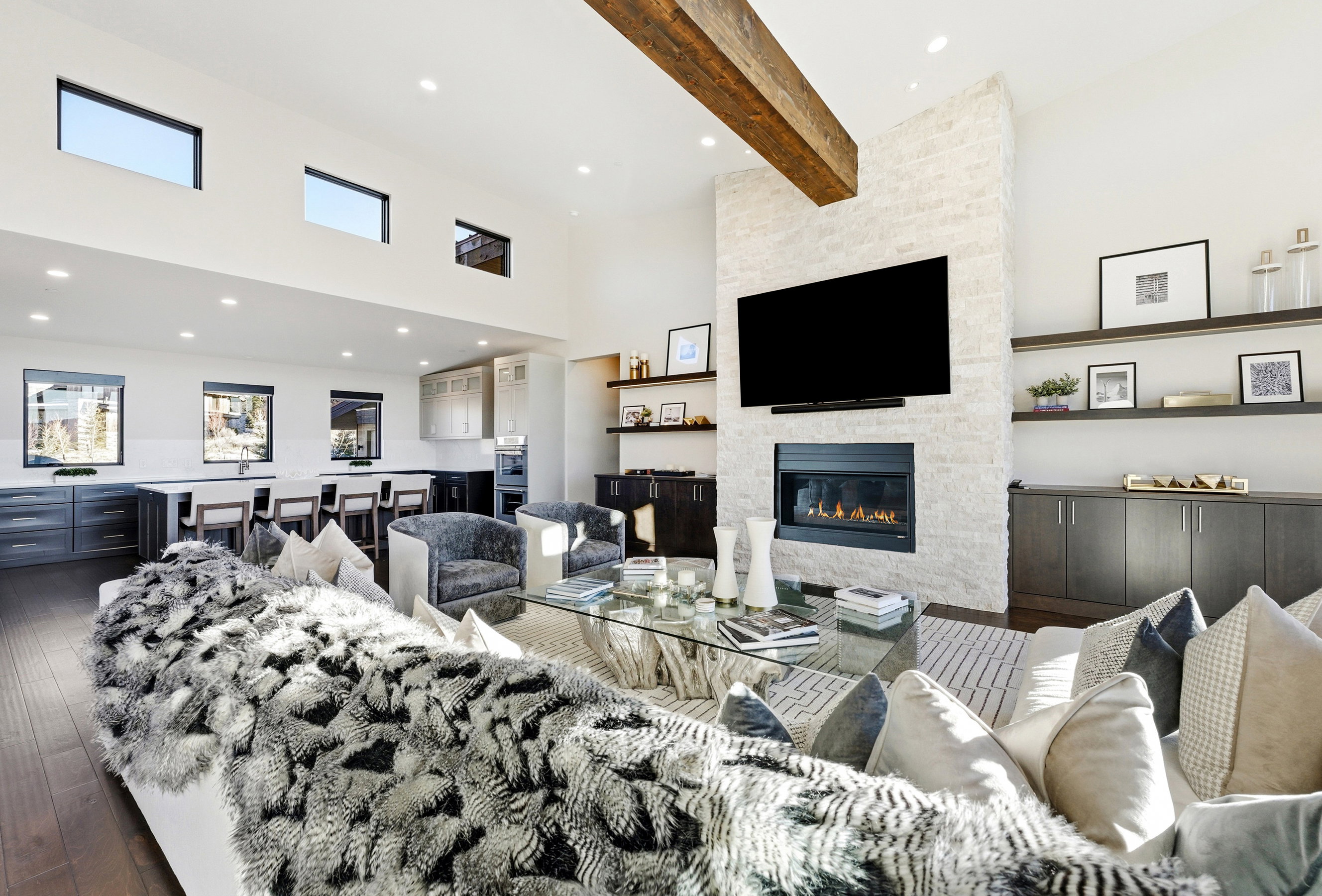Open-concept interior featuring high ceilings, exposed wood beam, a stone accent wall with a built-in fireplace, recessed lighting, and wood-finish flooring