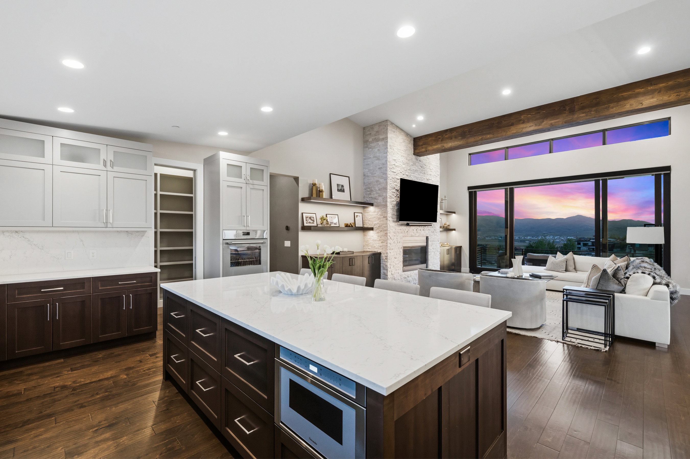 Open-concept living space featuring wood-finish flooring, a kitchen island with integrated microwave, a stone-clad fireplace with built-in shelving, and expansive sliding glass doors