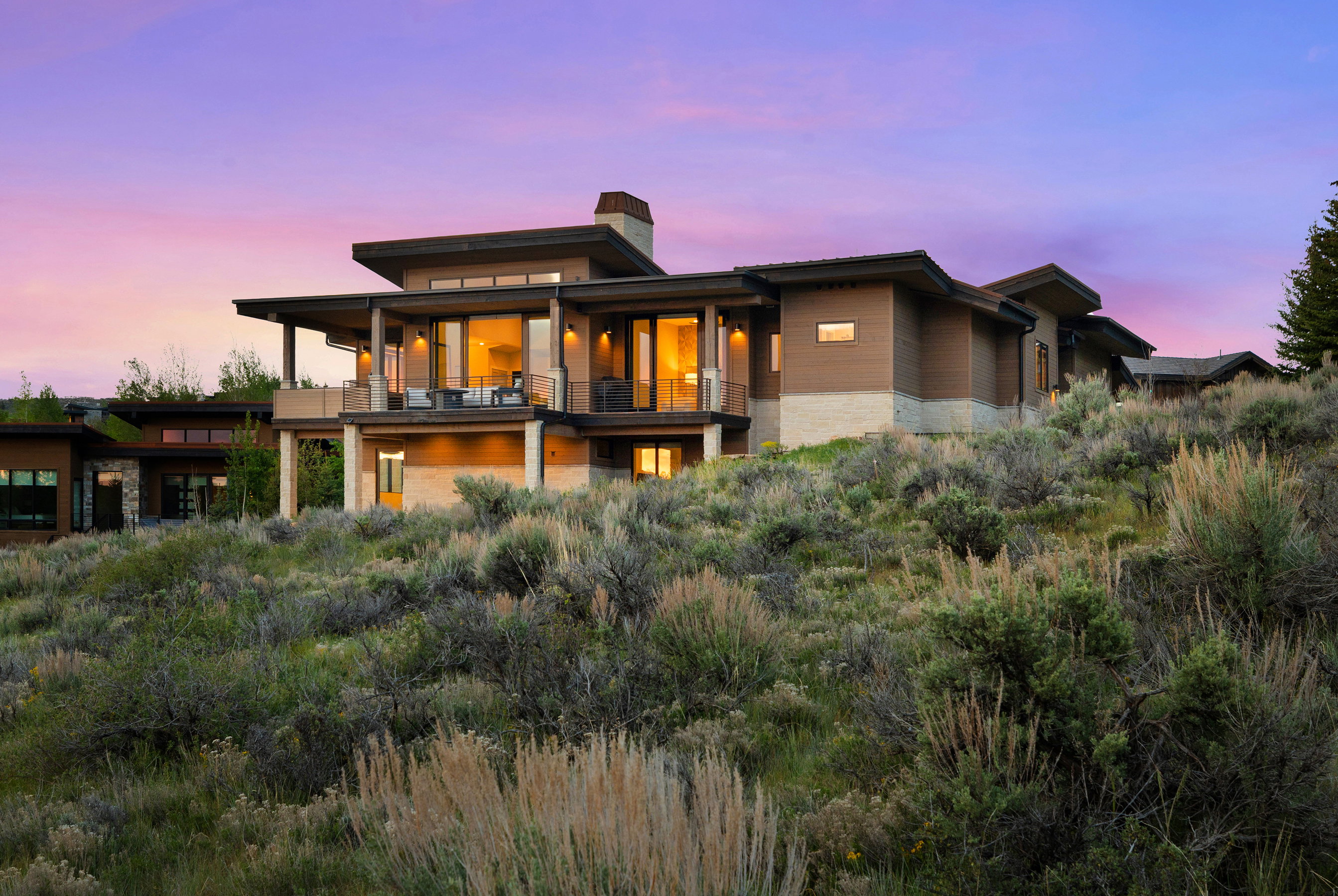 Contemporary multi-level residence featuring expansive glass panels, a stone-clad foundation, and multiple cantilevered balconies with dark railings