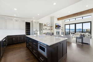 Kitchen featuring beamed ceiling, glass insert cabinets, light stone counters, dark wood-style flooring, and open floor plan