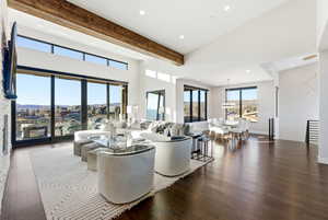 Living room with dark wood finished floors, beamed ceiling, a high ceiling, and recessed lighting