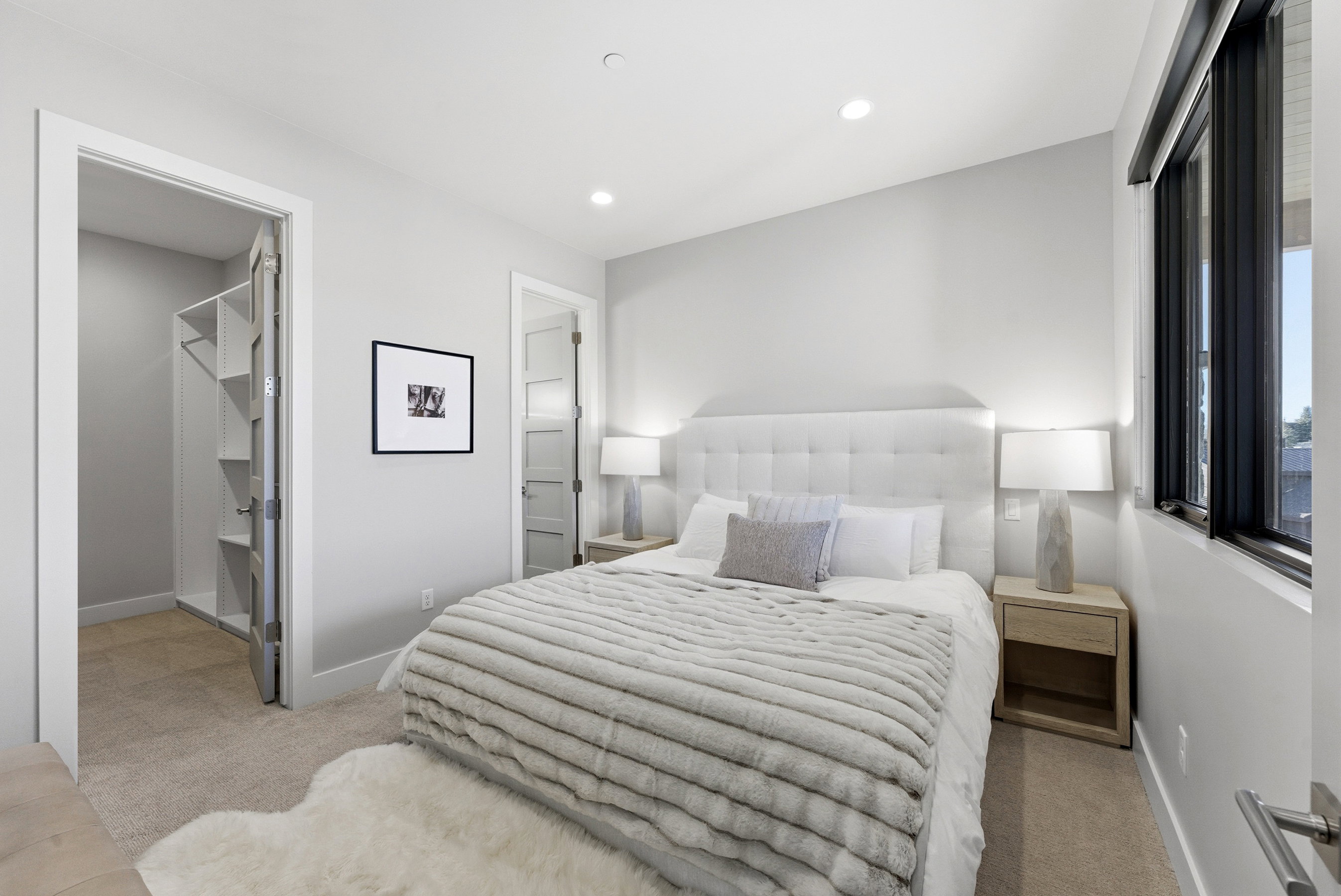 Carpeted room featuring a white upholstered headboard, recessed lighting, and a window with dark trim