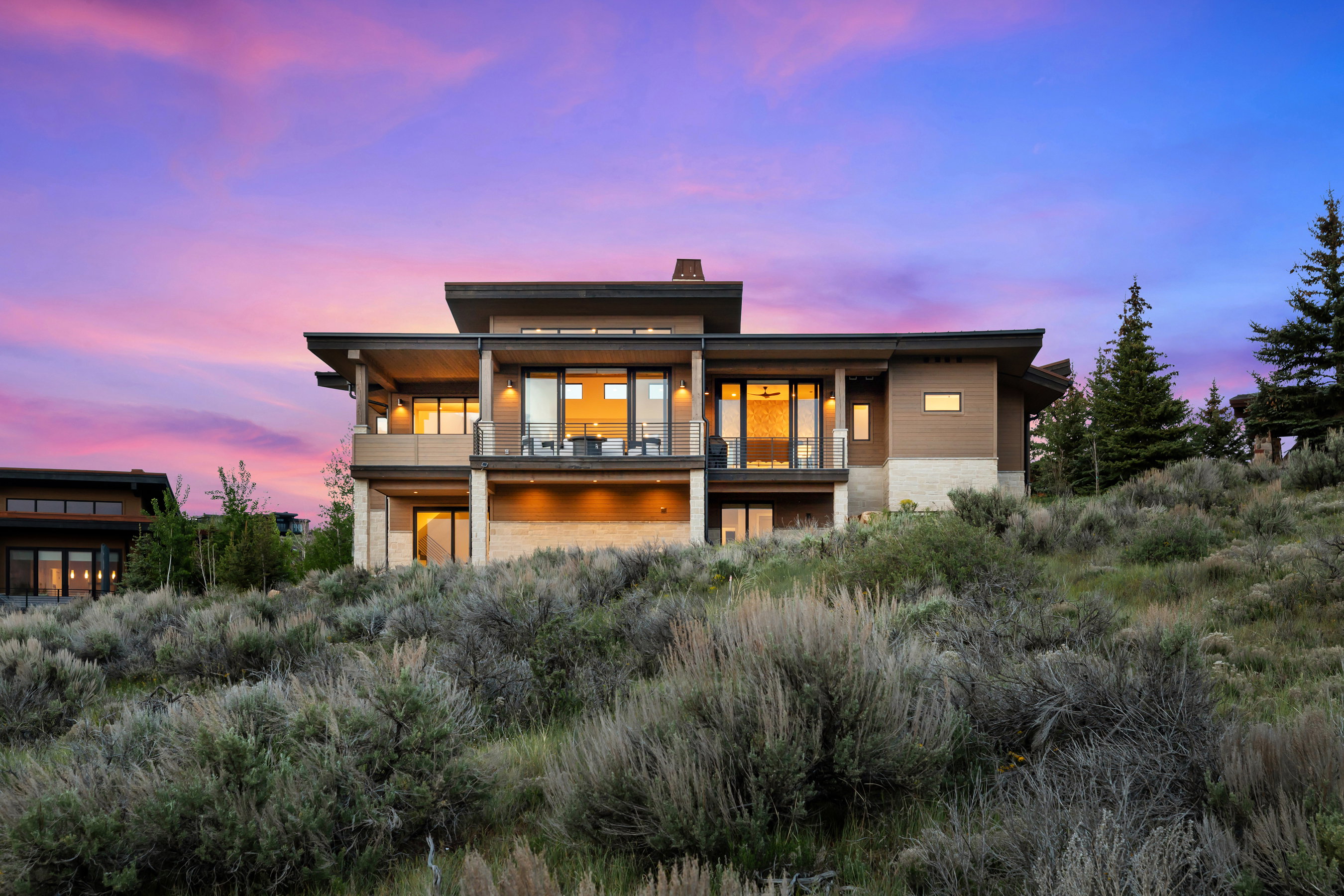 Modern multi-level residence featuring expansive glass doors, multiple covered balconies, and a stone facade