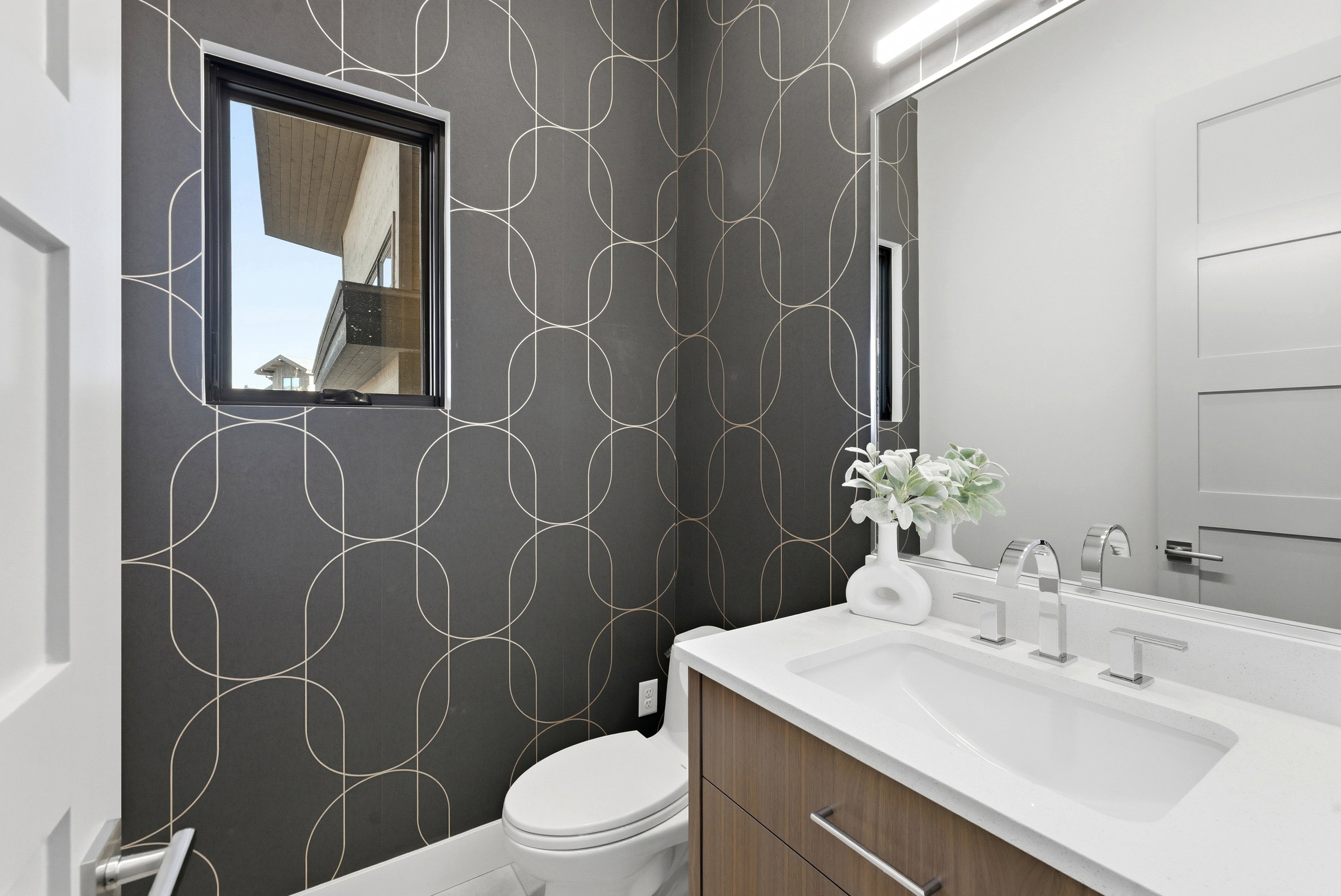 Powder room featuring a wood-finish vanity with a white countertop and integrated sink, chrome faucet, and a large wall-mounted mirror