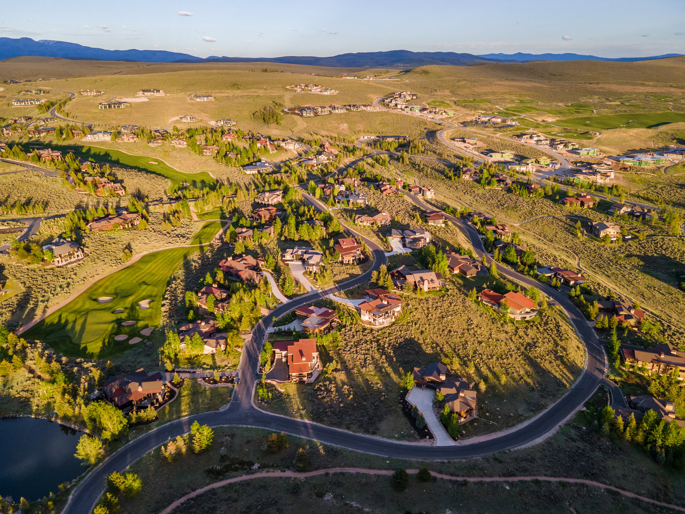 Aerial landscape featuring a residential community with winding roads, scattered trees, and a golf course