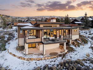 Snow covered back of property with a patio area, a chimney, and brick siding