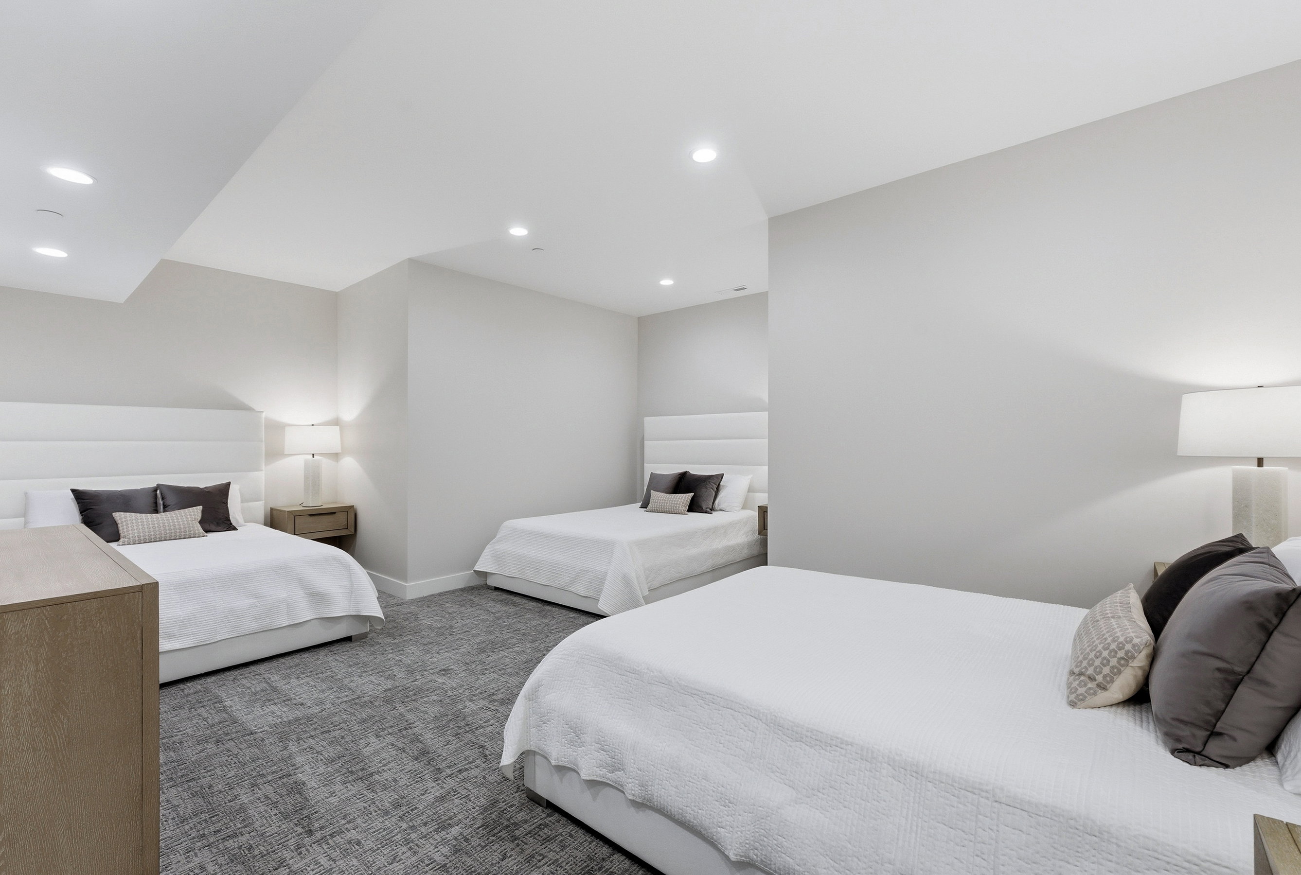 Spacious room featuring light gray walls, recessed lighting, and patterned gray carpeting