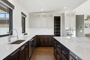Kitchen with light stone counters, dark brown cabinetry, appliances with stainless steel finishes, dark wood-style floors, and lofted ceiling