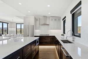 Kitchen featuring light stone counters, dark brown cabinetry, dark wood-style floors, glass insert cabinets, and stainless steel appliances