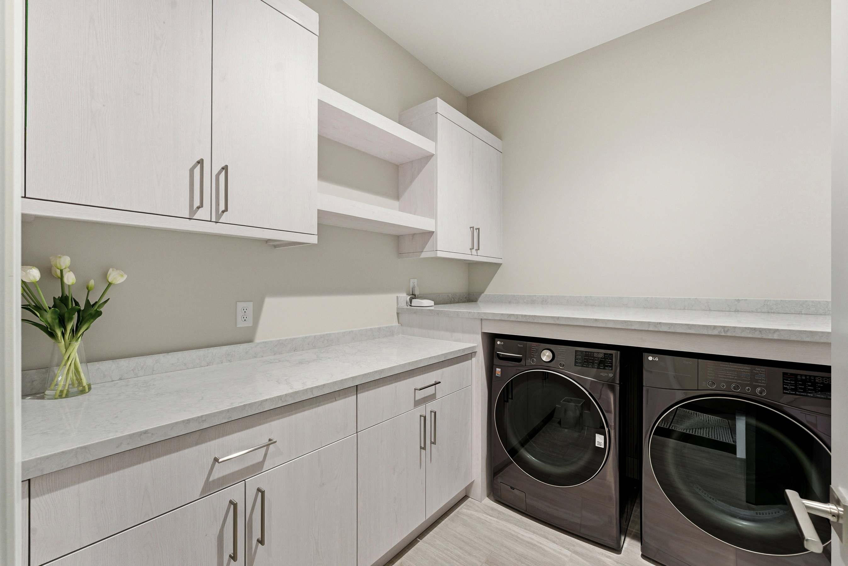 Dedicated laundry space featuring integrated countertop, light-toned cabinetry, two open shelves, and wood-finish flooring