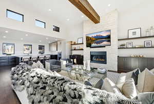Living room with a stone fireplace, a towering ceiling, beam ceiling, dark wood-type flooring, and recessed lighting