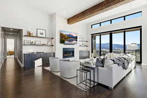 Living room featuring a high ceiling, beamed ceiling, a fireplace, dark wood-style flooring, and recessed lighting