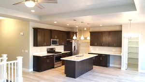 Same plan, previously built. Kitchen featuring stainless steel appliances, dark brown cabinetry, hanging light fixtures, an island with sink, and recessed lighting