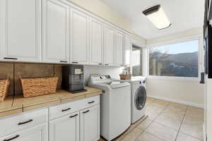 Laundry area featuring cabinet space, light tile patterned flooring, and independent washer and dryer