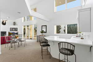 Kitchen with a breakfast bar area, a peninsula, light countertops, light colored carpet, and a high ceiling