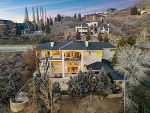 Back of property at dusk featuring a balcony, stairs, a chimney, stucco siding, and roof with shingles