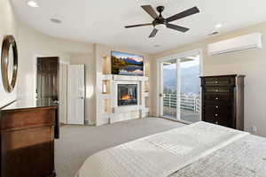 Bedroom with carpet flooring, access to outside, a wall mounted AC, ceiling fan, and a glass covered fireplace