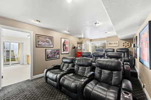 Home theater room with a textured ceiling and dark colored carpet