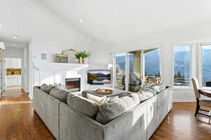 Living room featuring a lit fireplace, wood finished floors, and high vaulted ceiling