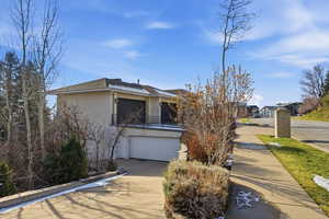 View of front facade with stucco siding, driveway, an attached garage, a balcony, and roof with shingles