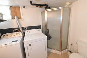 Washroom with light tile patterned floors, washing machine and dryer, and a textured ceiling
