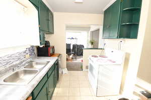 Kitchen with green cabinets, white electric range oven, light countertops, open shelves, and light tile patterned floors