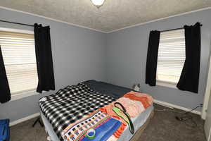 Bedroom featuring a textured ceiling, dark carpet, and crown molding