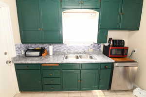 Kitchen featuring green cabinetry, light countertops, stainless steel dishwasher, and tasteful backsplash