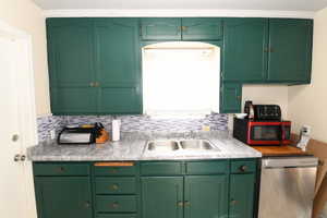 Kitchen with green cabinetry, light countertops, stainless steel dishwasher, and tasteful backsplash