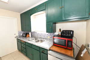 Kitchen featuring green cabinetry, light countertops, tasteful backsplash, and dishwasher