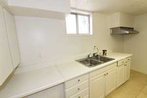 Kitchen with a textured ceiling, light countertops, white cabinetry, under cabinet range hood, and light tile patterned flooring