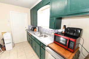 Kitchen featuring green cabinetry, light countertops, backsplash, and dishwashing machine