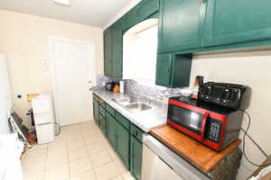Kitchen featuring green cabinets, light countertops, dishwasher, light tile patterned floors, and tasteful backsplash