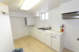 Kitchen with white cabinetry, light countertops, a textured ceiling, under cabinet range hood, and light tile patterned floors