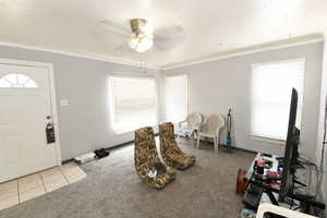 Foyer entrance featuring light colored carpet, ceiling fan, crown molding, and light tile patterned flooring