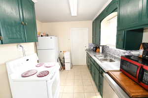 Kitchen featuring green cabinets, white appliances, light countertops, backsplash, and light tile patterned floors
