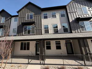 View of front of property with board and batten siding, brick siding, a shingled roof, and a fenced front yard