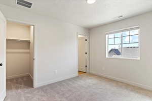 Unfurnished bedroom with a spacious closet, a textured ceiling, and light colored carpet