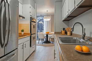 Kitchen featuring stainless steel appliances, decorative light fixtures, white cabinets, and light wood-style floors