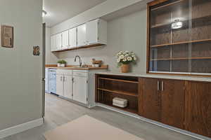 Bar featuring light countertops, white cabinetry, dishwasher, light wood-type flooring, and open shelves