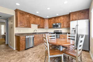 Kitchen with stainless steel appliances, dark stone counters, brown cabinetry, and recessed lighting