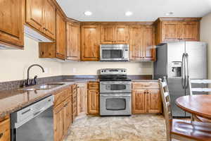 Kitchen with stainless steel appliances, dark stone countertops, brown cabinets, recessed lighting, and light tile patterned flooring
